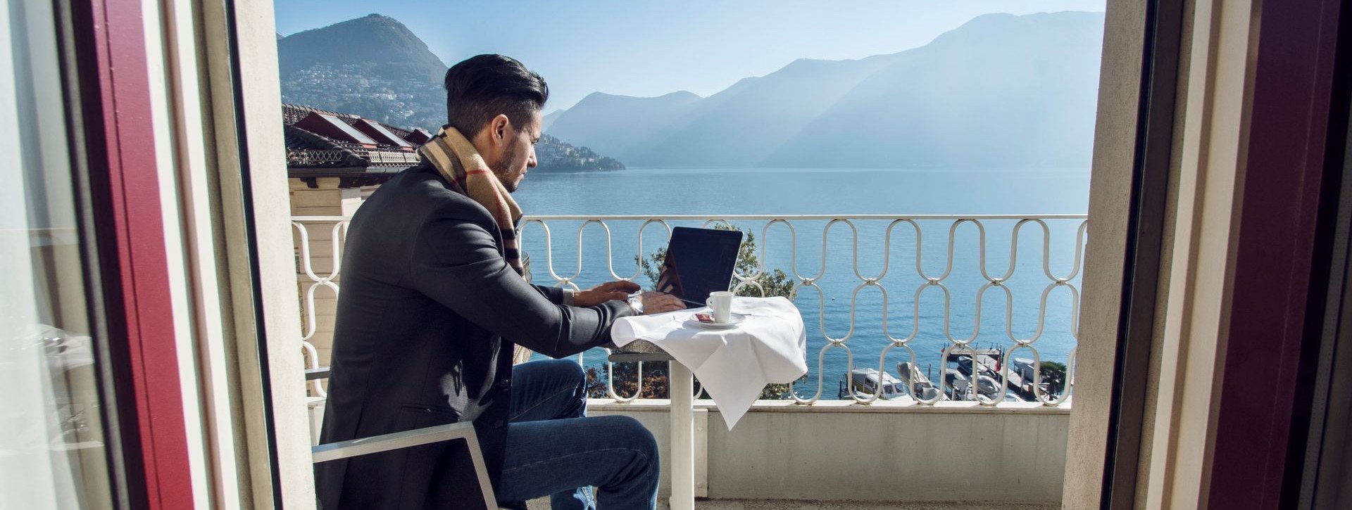 A man works on his notebook on the balcony with lake view